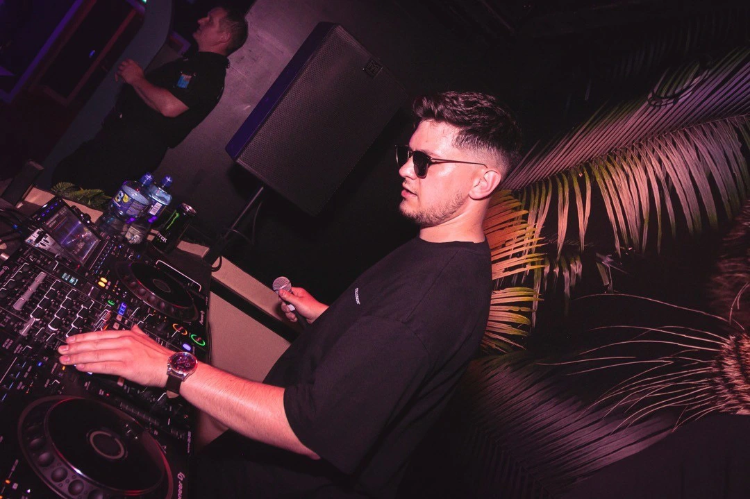 Robert Dani performing as a DJ at a live event, wearing headphones and operating turntables in a dynamic club environment with atmospheric lighting