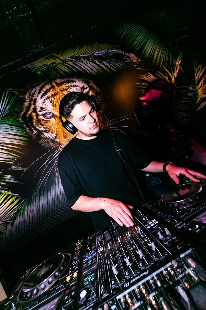 Robert Dani performing as a DJ at a live event, wearing headphones and operating turntables in a dynamic club environment with atmospheric lighting